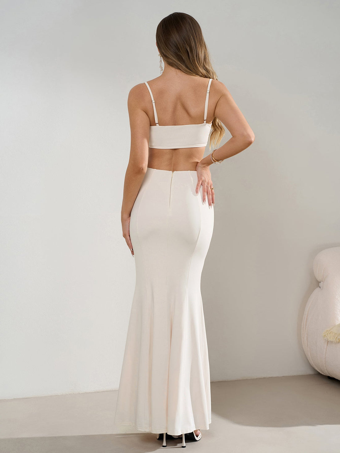 Woman wearing a white sleeveless mermaid evening gown with a square neckline, spaghetti straps, side cutouts, and a high slit.