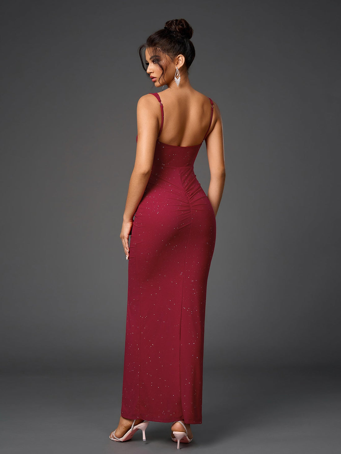 Woman wearing a floor-length, form-fitting, deep red dress with a sweetheart neckline, spaghetti straps, a midriff cutout, ruched detailing, and a high slit, adorned with subtle sparkling embellishments.