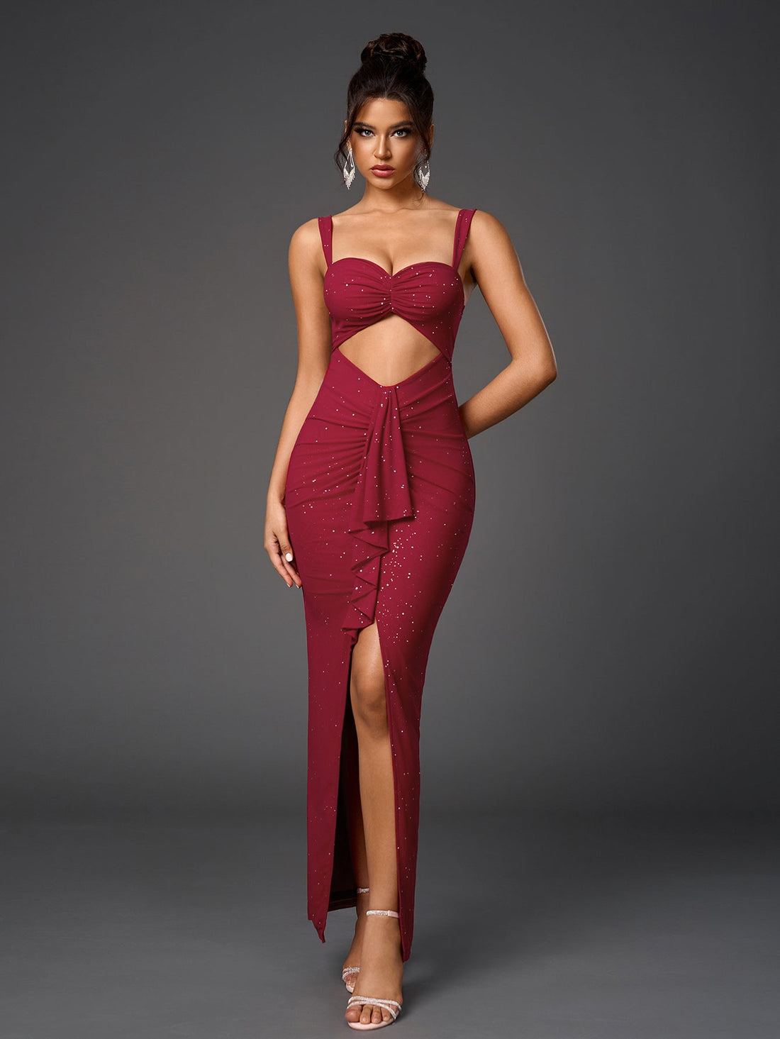 Woman wearing a floor-length, form-fitting, deep red dress with a sweetheart neckline, spaghetti straps, a midriff cutout, ruched detailing, and a high slit, adorned with subtle sparkling embellishments.