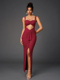 Woman wearing a floor-length, form-fitting, deep red dress with a sweetheart neckline, spaghetti straps, a midriff cutout, ruched detailing, and a high slit, adorned with subtle sparkling embellishments.