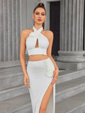 Woman wearing a white halter crop top with floral embellishments and a white high split maxi skirt