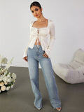 Full body shot of a woman in an ivory lace trim tie front top and jeans