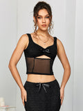 Front view of a model posing in a black textured knit cropped top with a sweetheart neckline, bow detail, and sheer mesh panel.
