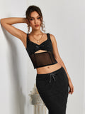Model leaning against a wall in a black textured knit cropped top with a sweetheart neckline and a sheer mesh panel.