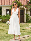 Full length shot of a woman in a white halter neck maxi dress holding a bouquet