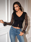 Woman wearing a black ruched V-neck crop top with lace sleeves and blue jeans