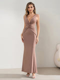 Model posing in a taupe fitted maxi dress with a V-neckline and tie back