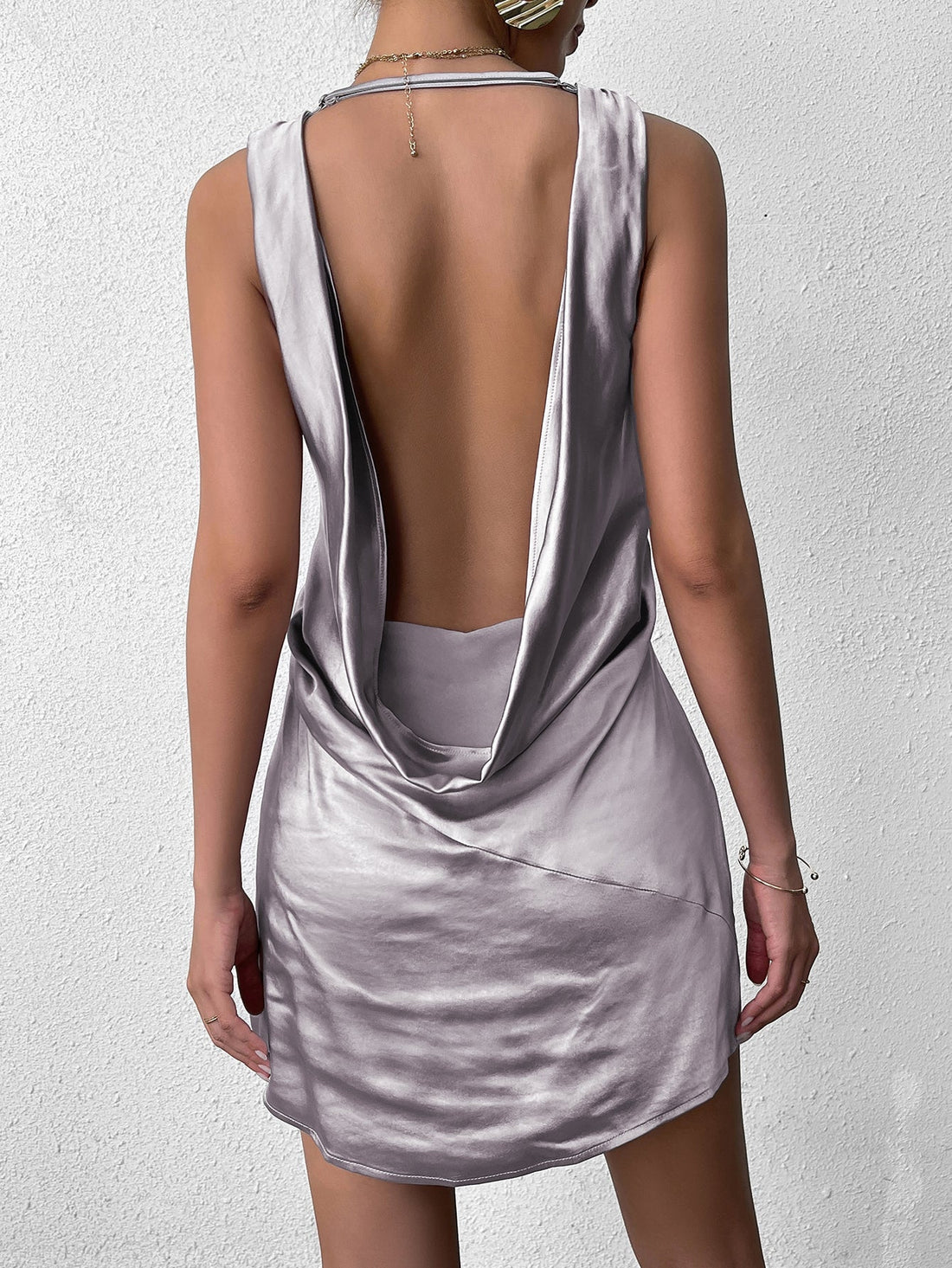Woman wearing a grey satin V-neck mini dress with a draped open-back.