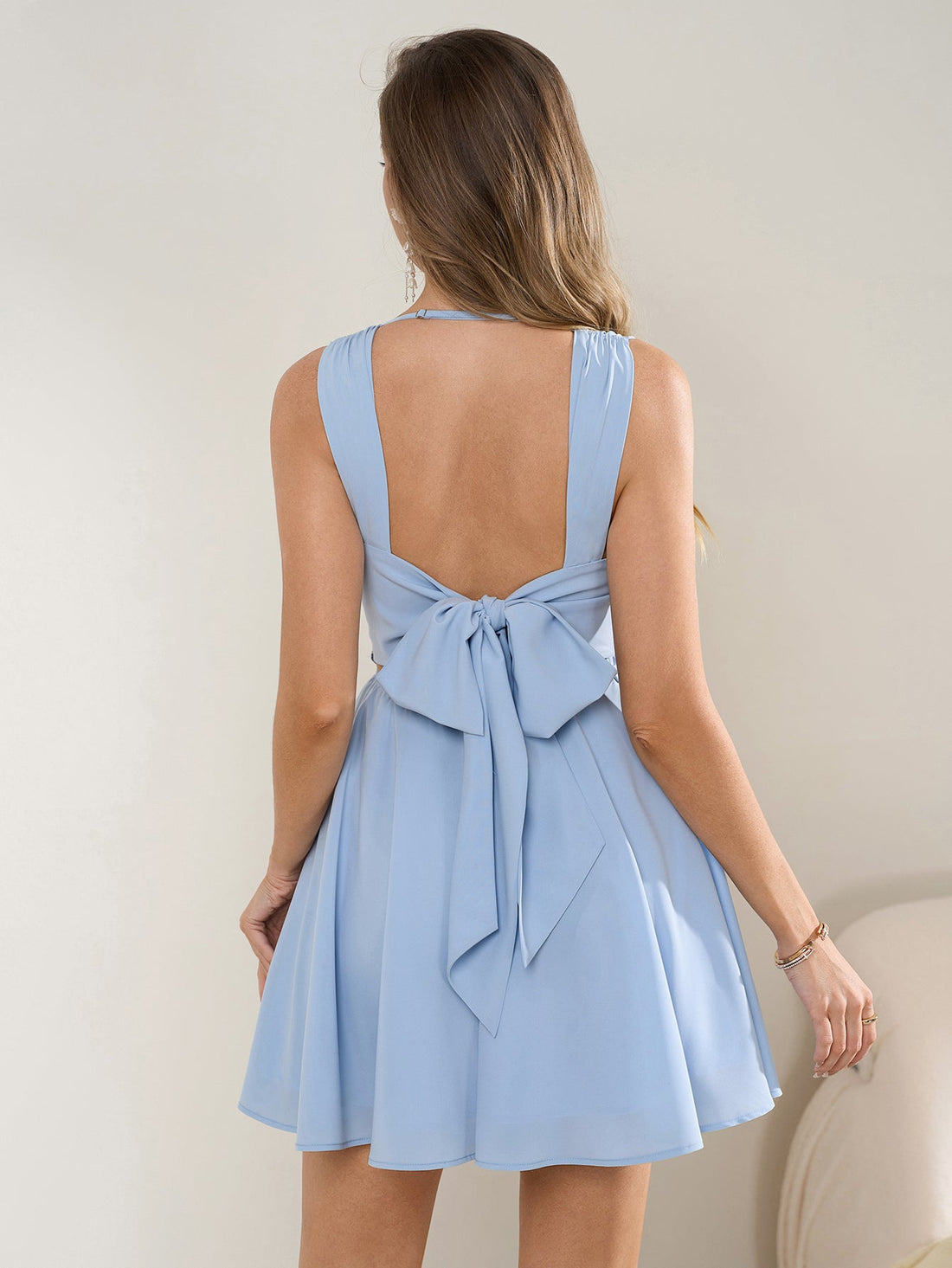 Woman in a light blue sleeveless cowl neck fit and flare dress with an open back and bow detail.