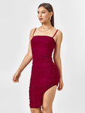 Side view of a woman in a red embellished ruched midi dress, highlighting the asymmetrical hem and fitted silhouette.