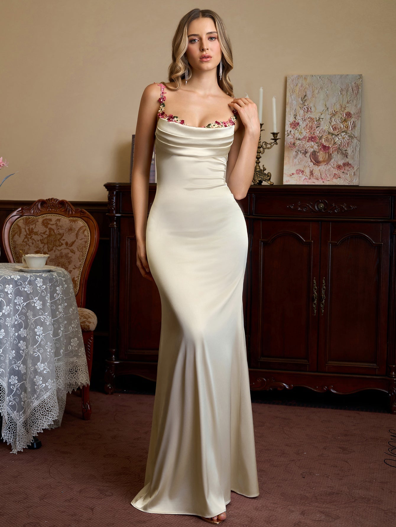 Woman wearing a cream satin evening gown with floral embellished straps and a cowl neckline