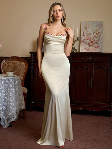 Woman wearing a cream satin evening gown with floral embellished straps and a cowl neckline