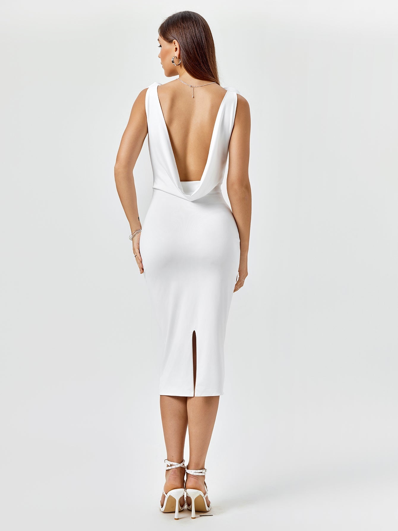 Back view of a white fitted midi dress with an open draped back and side slit