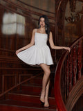 Model posing on stairs in a white A-line mini dress with spaghetti straps