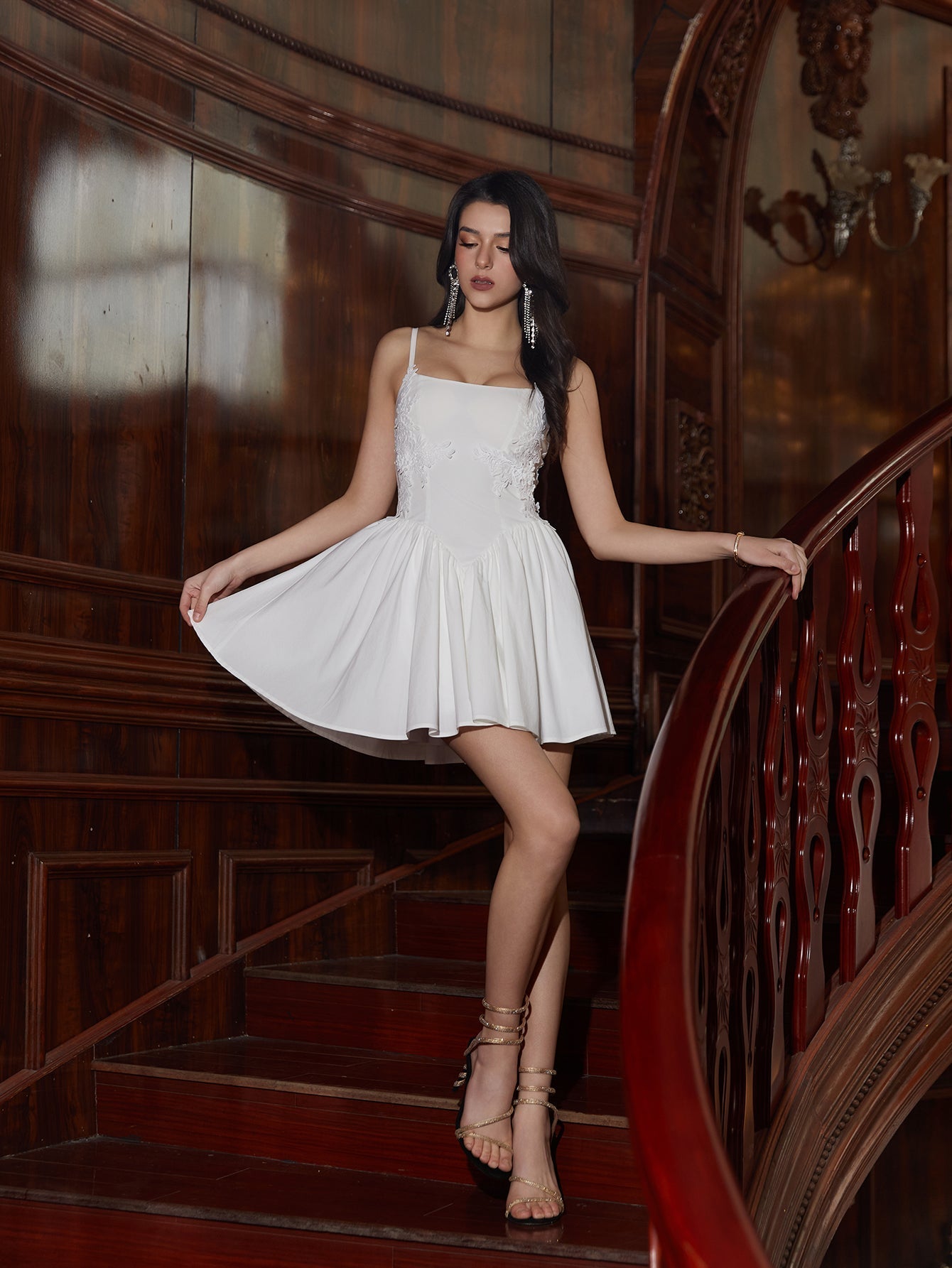 Model posing on stairs in a white A-line mini dress with spaghetti straps