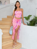 Woman holding a light blue handbag while standing on stairs in a pink floral print halter neck crop top and an asymmetrical ruffled midi skirt.