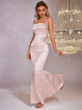 Woman wearing a light pink satin jacquard mermaid formal gown with a square neckline and adjustable tie straps.