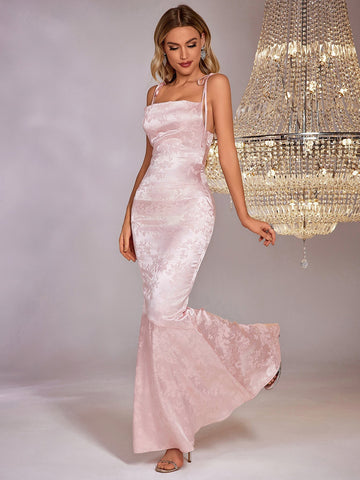 Woman wearing a light pink satin jacquard mermaid formal gown with a square neckline and adjustable tie straps.