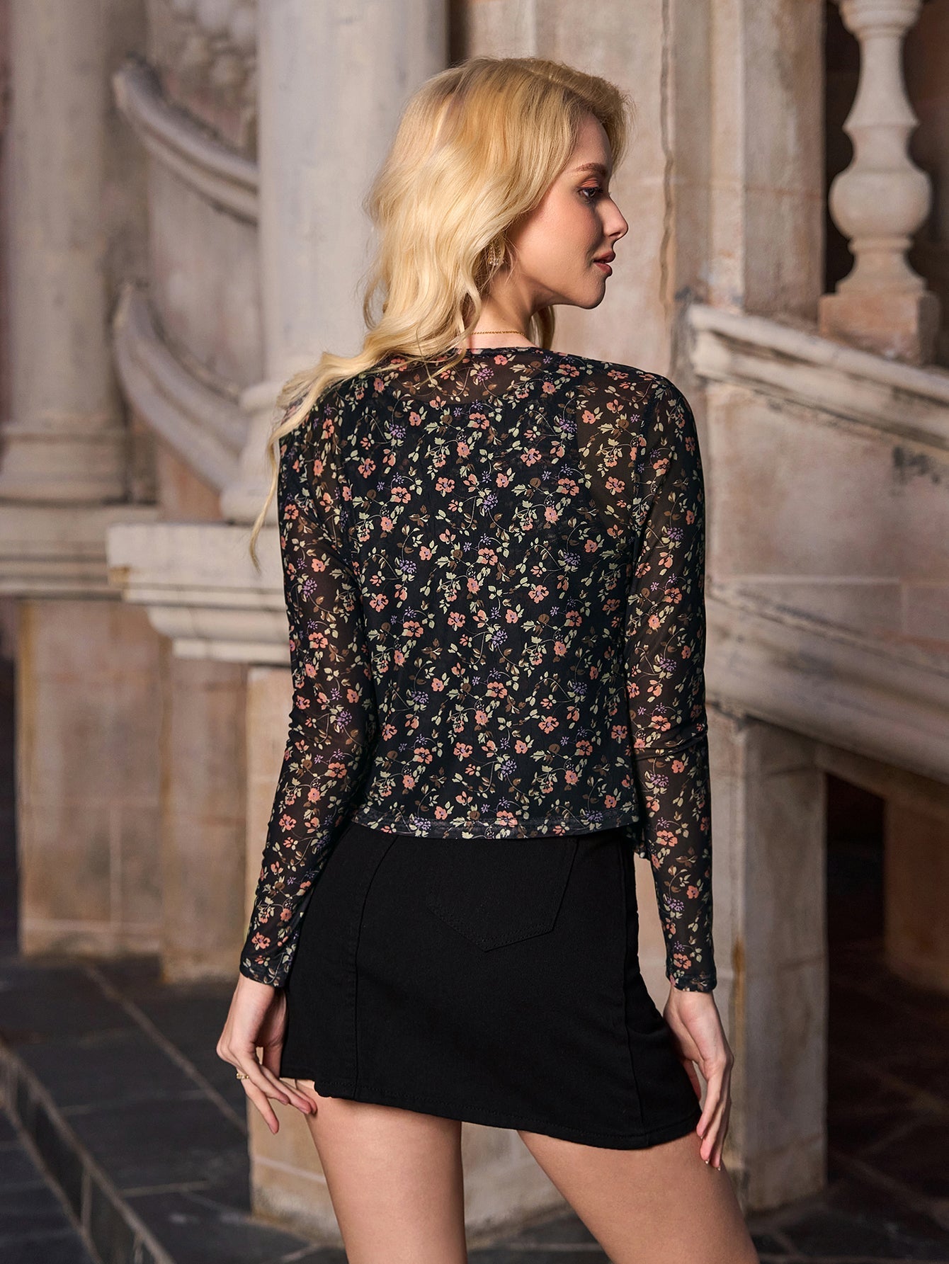Rear view of a woman wearing a black floral print sheer long sleeve cropped cardigan.