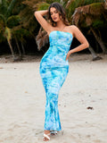 Woman with hand on hip wearing a strapless blue and white tie-dye print maxi dress with jellyfish graphic on a sandy beach with palm trees
