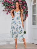 Woman in a white midi dress with blue floral print, sweetheart neckline, and tiered skirt, adjusting her necklace.