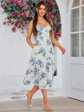 Woman in a white midi dress with blue floral print and side pockets, posing with one hand on her hip.