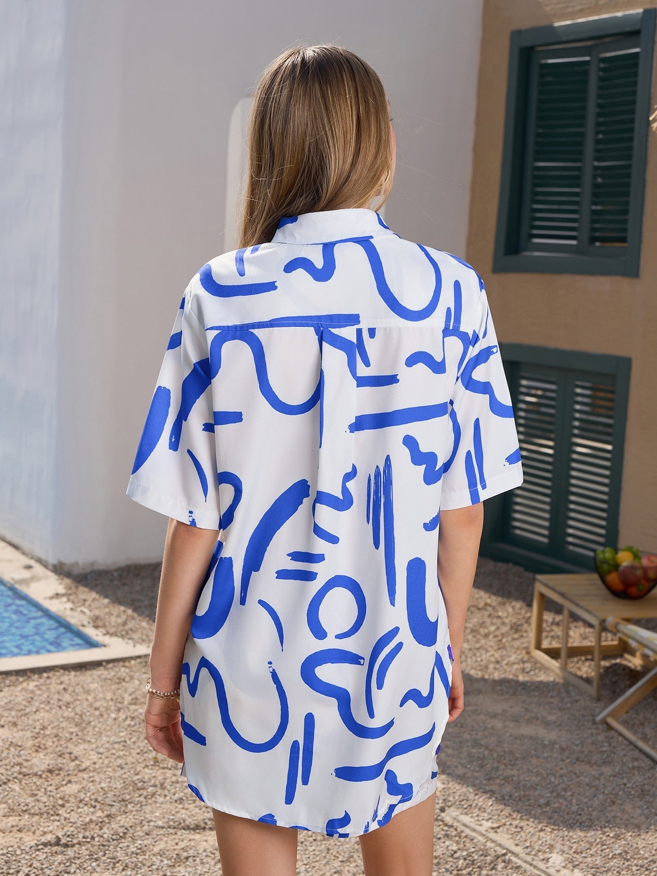Back view of a woman in a white short-sleeved button-down shirt with a blue abstract print.
