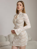 Side view of a woman wearing a white lace sheath dress with long bell sleeves and a tie-neck detail.