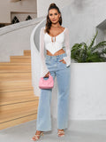 Woman holding a pink handbag while wearing a white tie-front crop top with sheer flared sleeves and light wash wide-leg jeans.