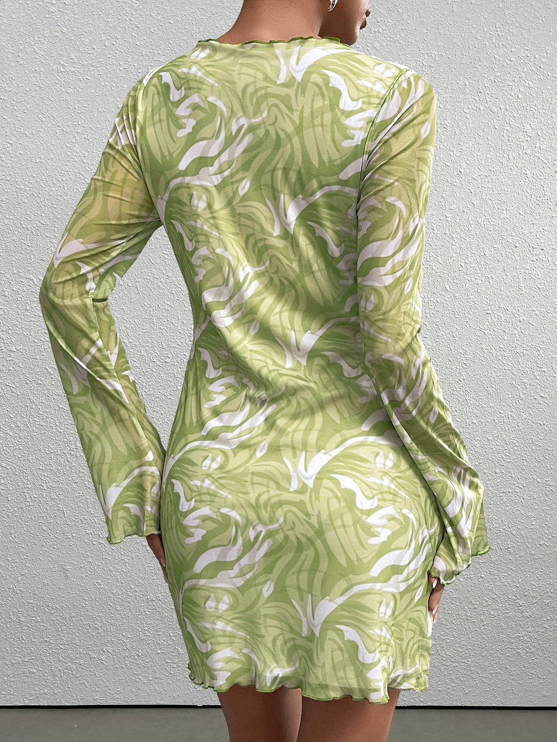 Woman wearing a green abstract print mesh mini dress with long sleeves