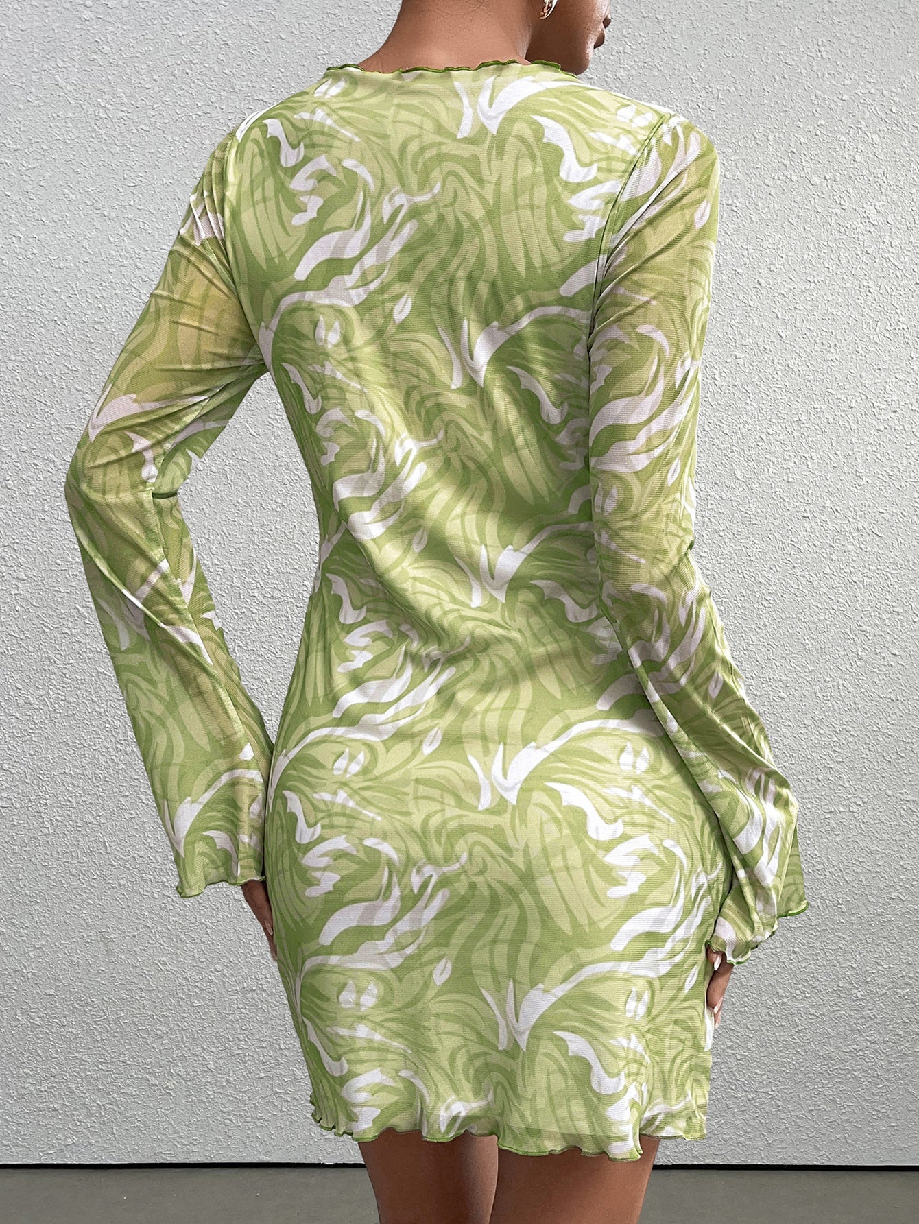 Back view of a woman in a green abstract print mesh mini dress