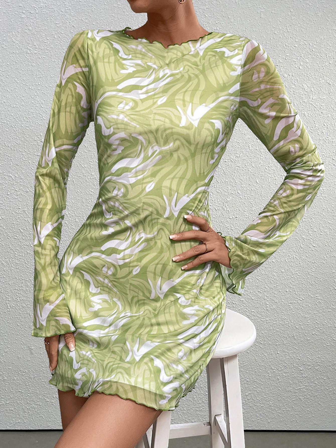 Woman wearing a green abstract print mesh mini dress with long sleeves
