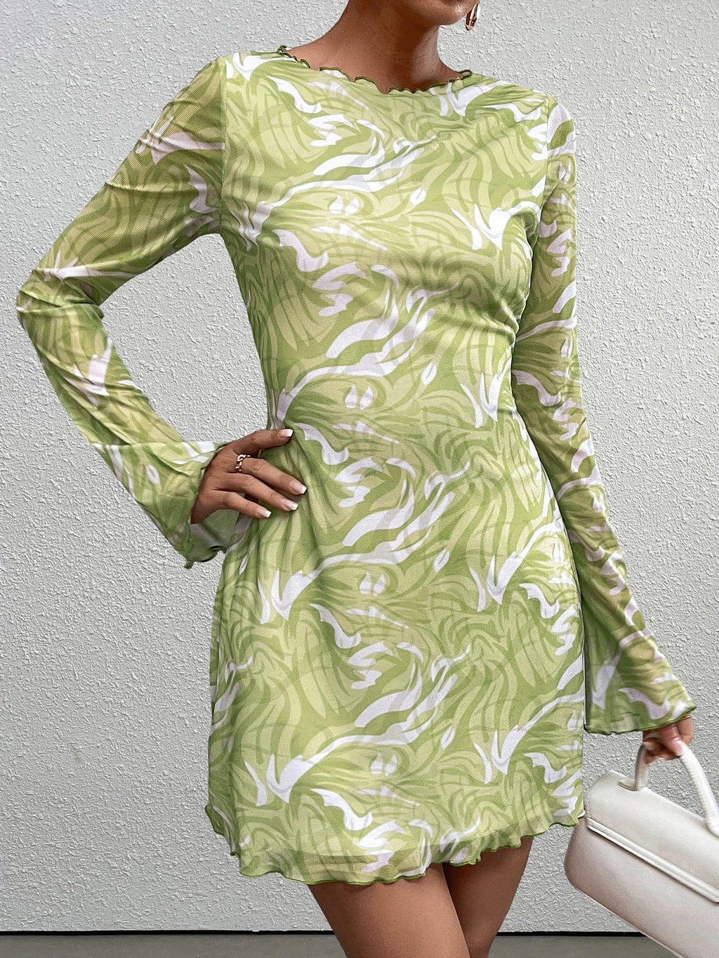 Woman in a green abstract print mesh mini dress holding a white handbag