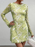 Woman in a green abstract print mesh mini dress holding a white handbag