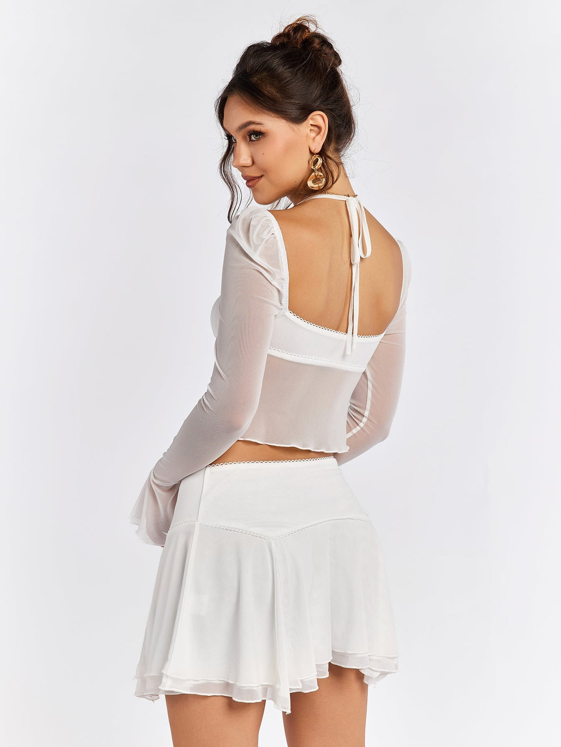 Woman wearing a white sheer mesh crop top with flared sleeves and a white mini skirt.