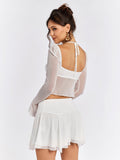 Back view of a woman in a white sheer mesh crop top and white mini skirt.