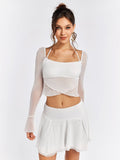 Woman wearing a white sheer mesh crop top with flared sleeves and a white mini skirt.