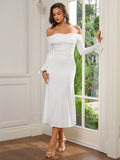 Woman leaning against a doorframe in a white off-the-shoulder midi dress with long flared sleeves.