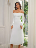 Full-length shot of a woman in a white off-the-shoulder midi dress, standing by a window.