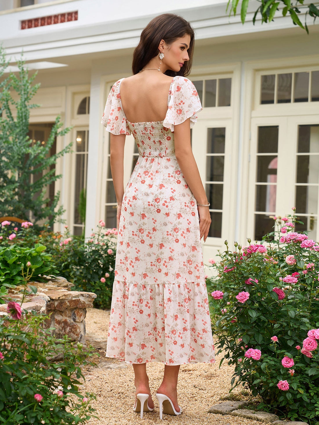 Woman wearing a white floral print midi dress with flutter sleeves and a tiered skirt.