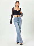 Full body shot of a woman wearing a black mesh long-sleeve crop top and light wash wide-leg jeans, holding a handbag.