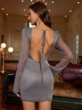Back view of a woman in a silver sparkly long sleeve bodycon dress with an open tie-back detail