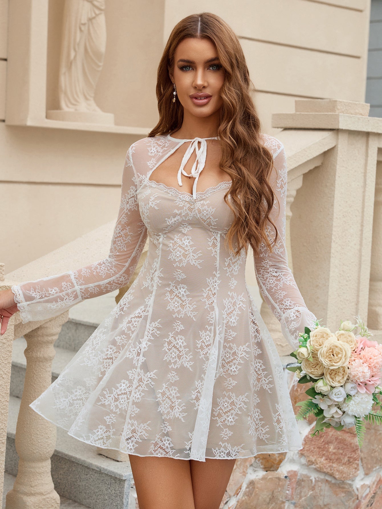 Woman in a white lace mini dress holding a bouquet of flowers, standing on outdoor stairs.