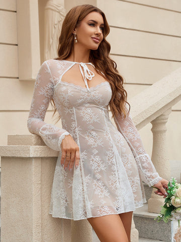 Woman wearing a white lace mini dress with long bell sleeves and a tie-neck detail, posing on stairs.