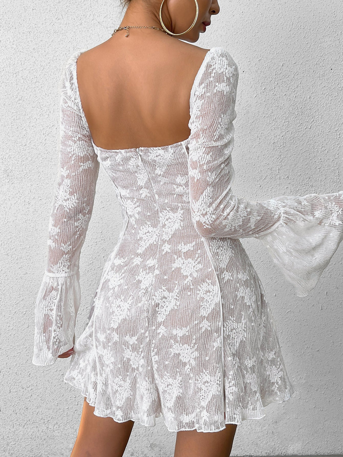 Woman wearing a white lace mini dress with long bell sleeves and a square neckline