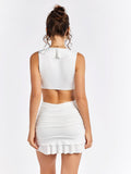 Back view of a woman in a white sleeveless mini dress with a deep V-neck, ruffle trim, and cut-out details