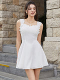 Woman wearing a white sleeveless fit and flare day dress with a square neckline and ruffled trim