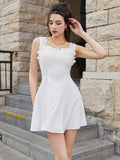 Woman posing in a white sleeveless fit and flare day dress with a square neckline and ruffled trim