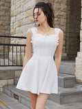 Front view of a woman in a white sleeveless fit and flare day dress with a square neckline and ruffled trim