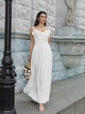 Woman in a white maxi dress with ruffled trim and spaghetti straps holding a bouquet of flowers.